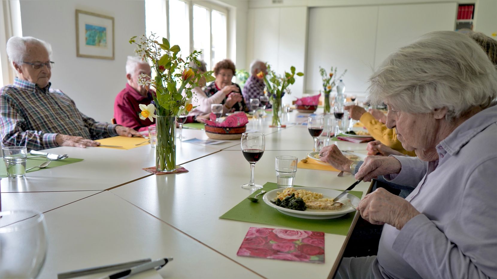 Senioren essen zusammen an einem langen Tisch.